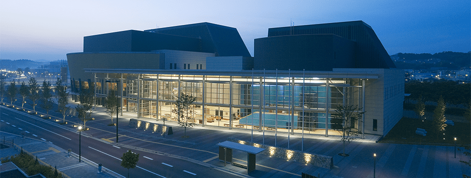 三田市総合文化センター郷の音ホールの公式施設外観写真。夜間の建物と前面道路を示す案内画像。