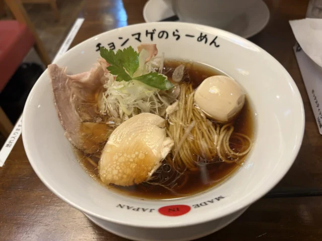 店名入りの白い器に、肉、卵、ねぎなどが盛られたラーメン
