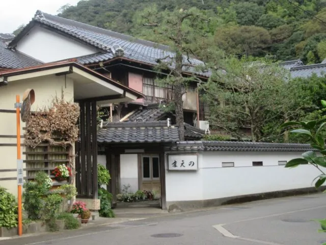 旧まえの旅館の外観。白い塀、瓦屋根の門と木造2階建ての建物