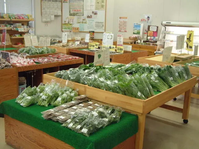 緑のマットを敷いた木製の平台に野菜が並ぶ西谷夢市場の売場