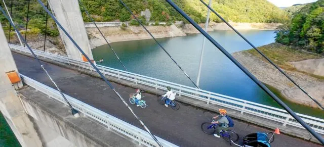 つくはらサイクリングターミナル周辺の、湖にかかる橋を自転車で走る人たちの写真