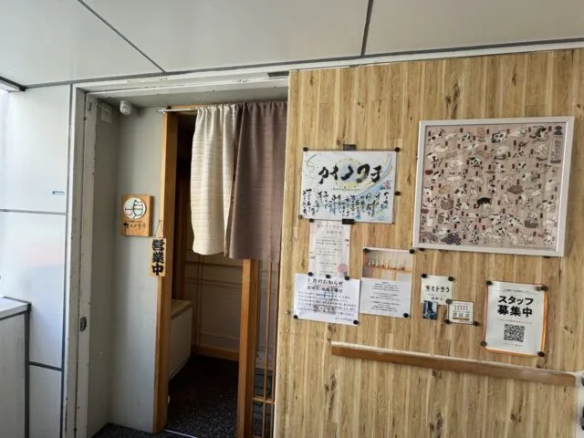 入口全景。同じカイノクチ店名・暖簾・木壁に猫の絵と採用掲示。（2025年1月7日撮影）