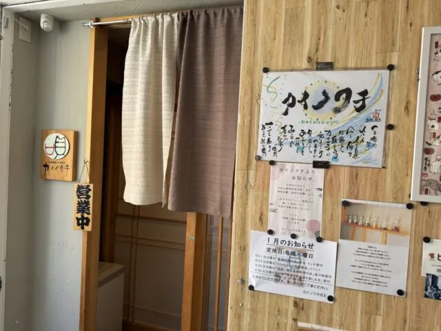 入口のカイノクチ店名、茶色の暖簾、明るい木壁と営業中札。（2025年1月7日撮影）