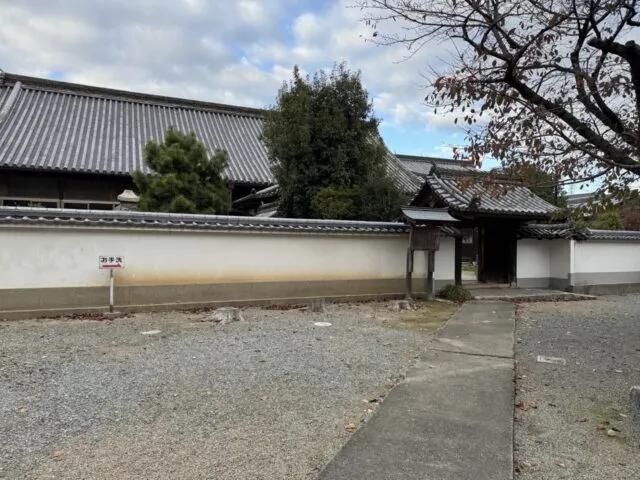 白い土塀と瓦屋根の門。お手洗いの案内も写っています。