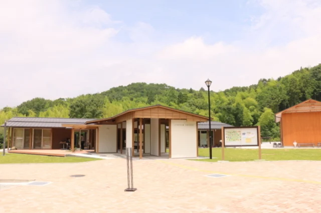 丸尾建築総合公園内の体験学習施設。茶色い木の屋根と白い壁の平屋建てで、前に広場がある