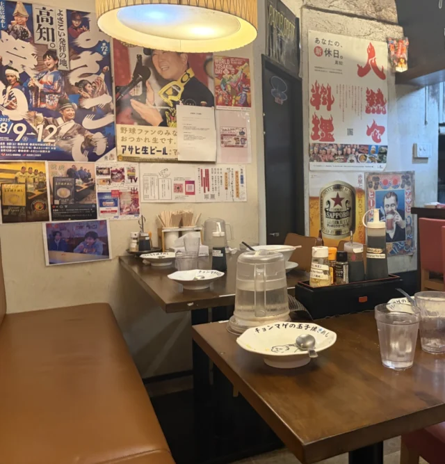 店内のテーブル席と店名入りの皿、壁の高知関連のポスター