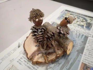 松ぼっくりや木の実を組み合わせ、木の台に乗せた動物の置き物の作品例