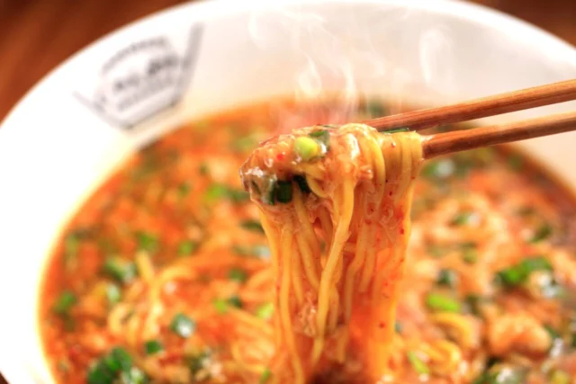 公式のジャン麺写真。赤橙色のあんにニラと卵が入り、持ち上げた麺に絡んでいる