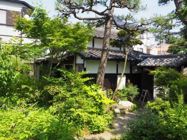 富田砕花旧居の外観。庭の草木の奥に、白壁と濃い木部、瓦屋根の建物がある。