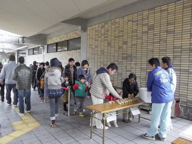 建物前の机で食べ物を渡す人と来場者。公園が紹介する過去のふるまいの様子
