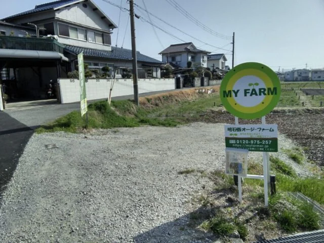 明石西オージー・ファーム入口の砂利道と緑色の丸い案内看板
