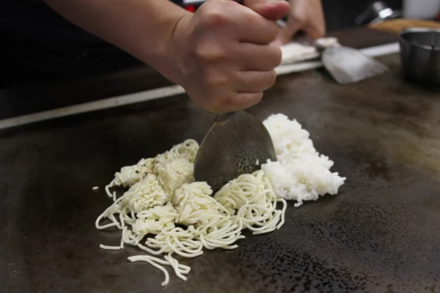 鉄板の上で麺とご飯をコテで合わせる、青森のそばめしの調理工程