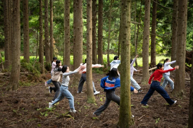 城崎国際アートセンターが公開した制作関連写真。緑に囲まれた屋外で動くこどもダンサーたち