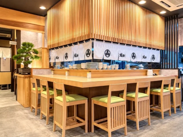 白木のカウンターと縦格子、白い暖簾、松の盆栽がある改装後の店内