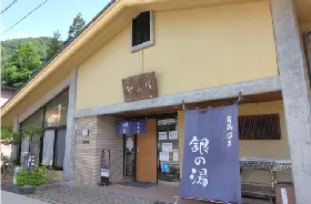 銀の湯の低い建物、淡い色の壁と青紫の暖簾