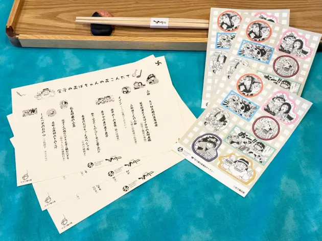 公式特典イメージ。キャラクター入りのお品書きとオリジナルシール