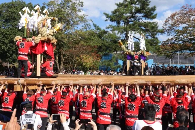 多くの担ぎ手が長い木材を支え、その上に飾りを付けたやぐらが載る出石だんじりの紹介写真