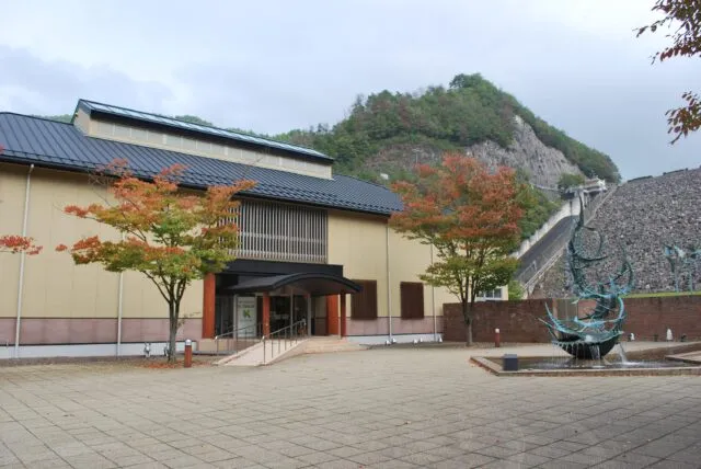 あさご芸術の森美術館の外観。黒い屋根、淡い黄色の外壁、入口の階段とスロープ。