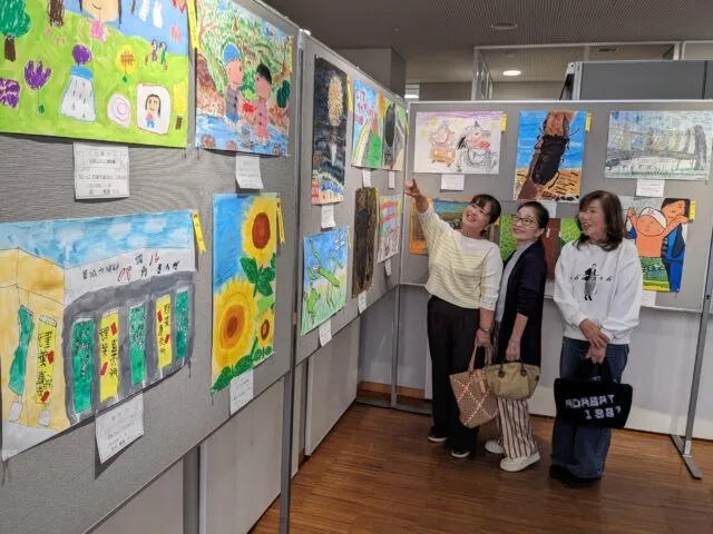 公式の展示イメージ。花・昆虫・身近な店などを描いた絵画が展示パネルに並ぶ