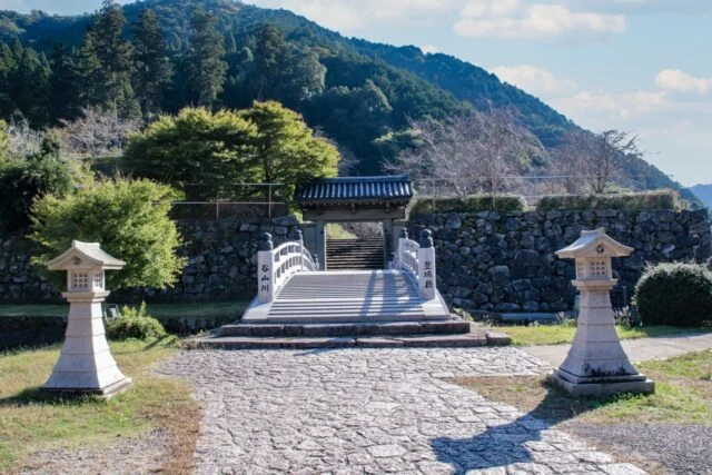 兵庫観光ナビ掲載の出石城跡。石畳の先に登城橋と門、奥に石段が続き、左右に自然石の石垣が見える