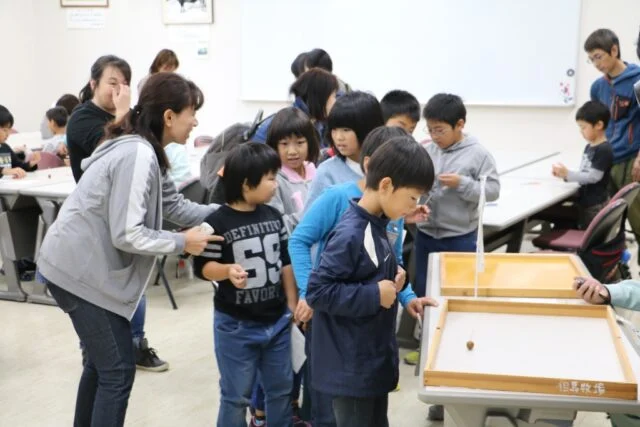 但馬牧場公園が掲載する過去の大会の様子。競技台のどんぐりごまを参加者が見守る