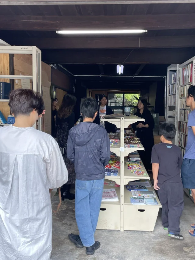 主催者が公開する江原のオモテ屋。木の梁や本棚、中央の棚がある室内に人が集まっている。
