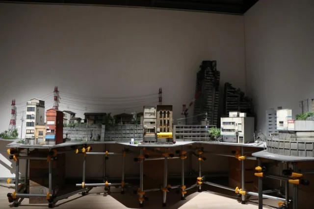 TokyoBuildの作品と東宝映像美術によるジオラマ。模型の街並みや架線、展示を支える構造が見える