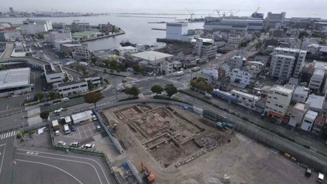 海沿いの市街地で、長方形の掘削区画と建物跡が見える兵庫津の発掘調査地の航空写真