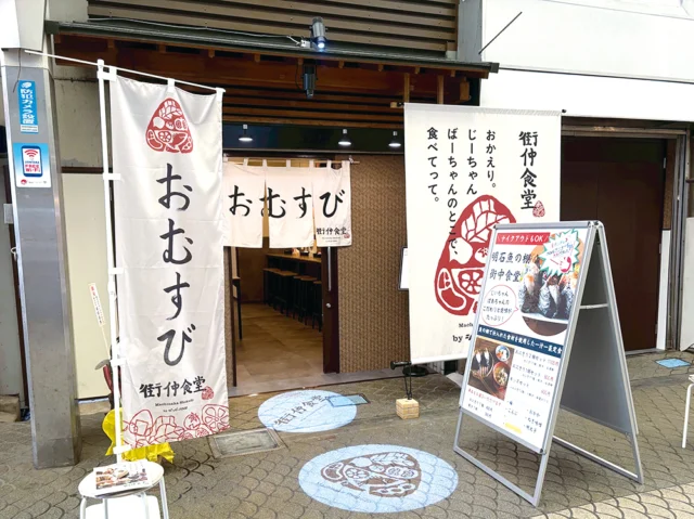 おむすびの白いのれんと赤い紋の旗がある明石魚の棚 街仲食堂の入口