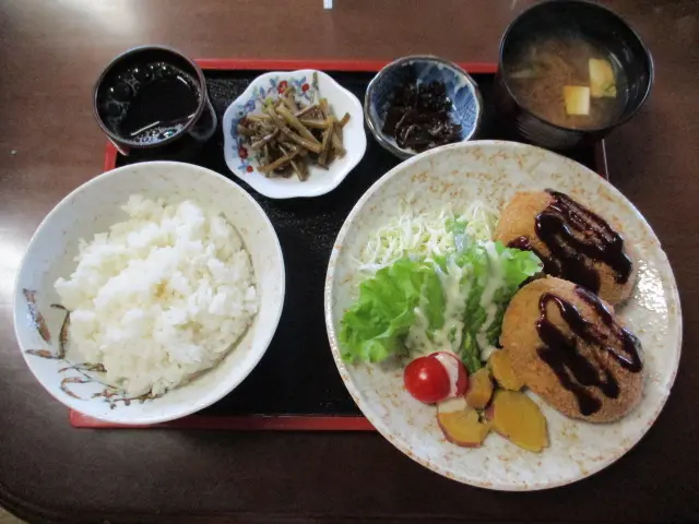 ドライブインオアシスのコロッケ定食の掲載写真。丸いコロッケ2個、野菜、ご飯、味噌汁、小鉢