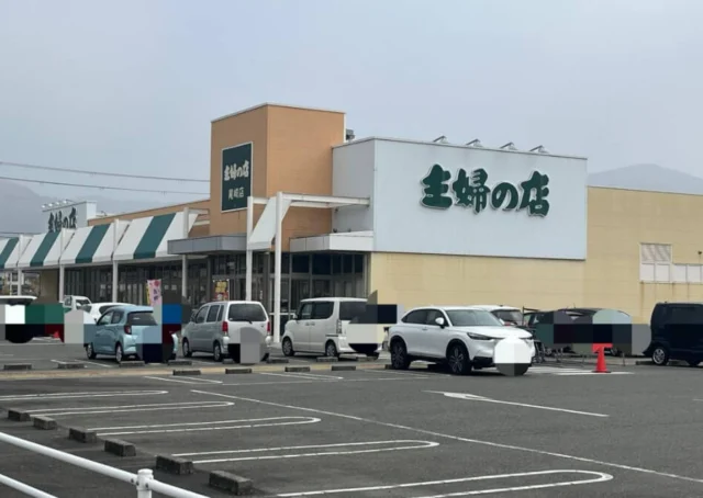 主婦の店尾崎店の外観。白い看板面と黄土色の建物、緑と白の日よけ
