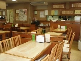 東京庵の店内。木のテーブルと背もたれのある椅子、奥のカウンター