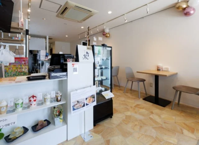 店舗公式の店内写真。白いカウンターとショーケース、右側の壁際にテーブル席が並ぶ