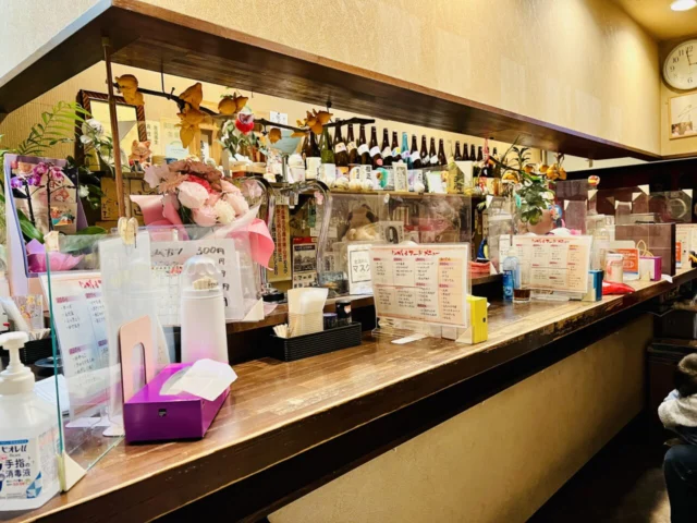 おみぞ筋商店街の公式店舗紹介に掲載された、じゃがいもの木製カウンターと酒瓶が並ぶ店内。掲載当時の様子