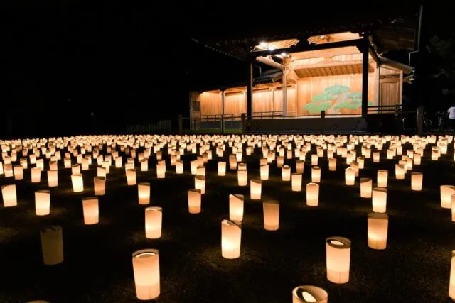 たかさご万灯祭2025、高砂神社の舞台の前に低い筒形の灯りが並ぶ様子