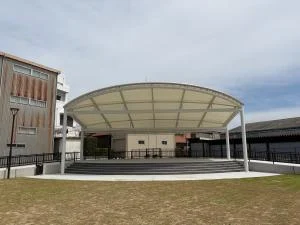 市コミュニティパークの芝生に面した白いアーチ形の屋外ステージ