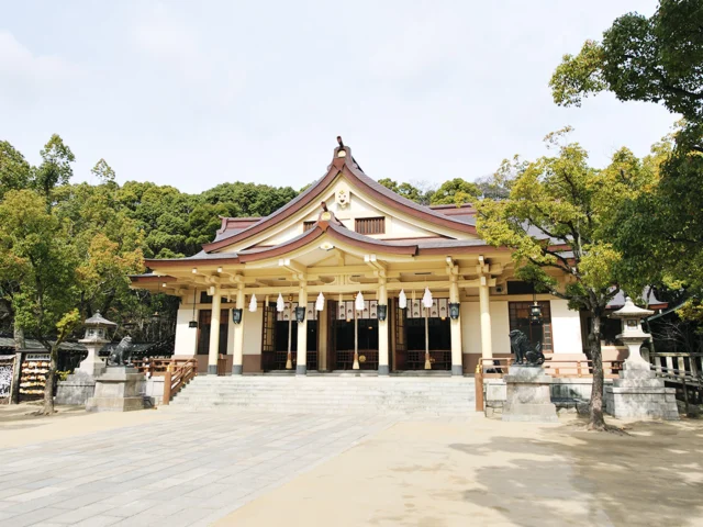 緑の木々の前に建つ湊川神社の白い柱と褐色の屋根の社殿