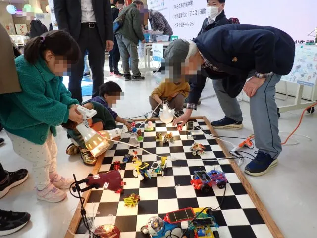 2026年春の同名フェアで、照明を当てたおもちゃを囲んで体験する様子