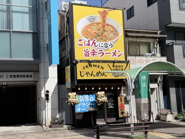 じゃんめん神戸板宿店の外観。黄色い大きな看板と店舗入口、休止中のバス停が見える