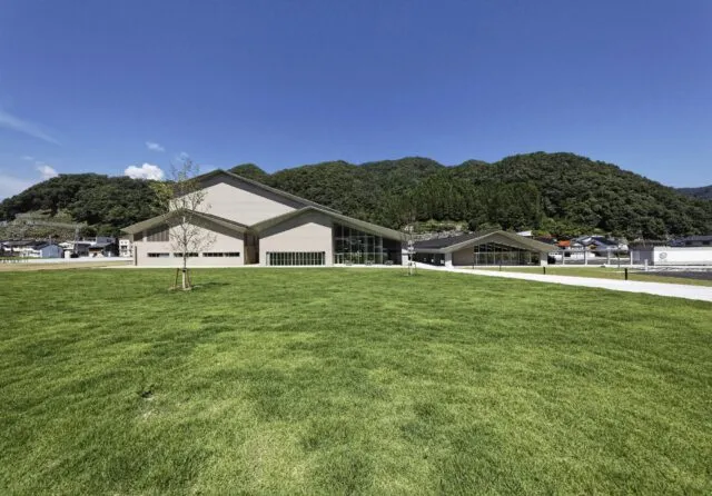 やぶ市民交流広場の芝生と、白い切妻屋根のホール棟。施設紹介の写真で、2026年の展示記録ではありません。